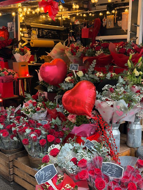 A floral display outside Woodford Florist showcasing an assortment of fresh flowers, predominantly red roses and white sprigs, arranged in baskets, vases, and bouquets. Among them are large, shiny red